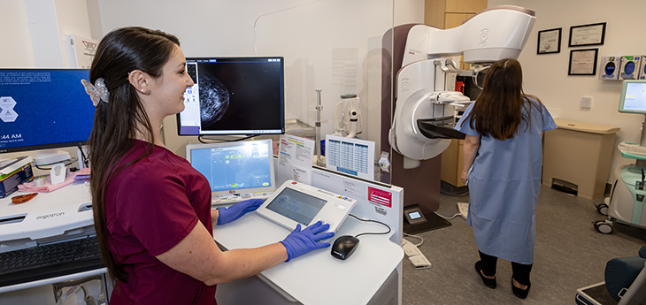 Woman in a red uniform assisting a patient during a mammogram in a medical imaging room.